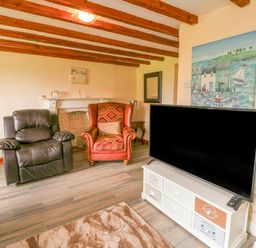 A living room with wooden beams leather and fabric armchairs a flat screen tv on a stand and a painting on the wall at The Linhay in Holsworthy