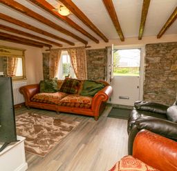 A living room with a leather sofa armchair a television a mirror and exposed wooden beams at The Linhay in Holsworthy