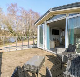 An outdoor wooden deck with wicker chairs and a glass table adjacent to a living room with sofa and TV at 109 Pentney Lakes in Pentney near King's Lynn
