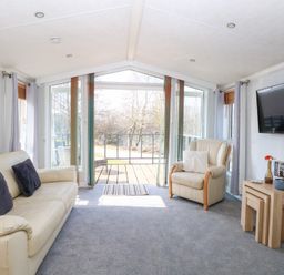 A living room with beige sofas a mounted television and sliding glass doors opening to a balcony at 109 Pentney Lakes in Pentney near King's Lynn