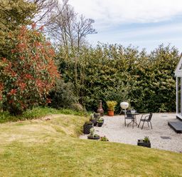 A garden area with patio furniture and potted plants next to a glass conservatory at The Old Vicarage Retreat in Luxulyan