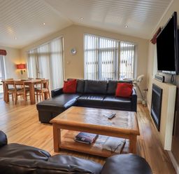 A living room with a black leather sofa and red cushions a wooden coffee table a dining table set and a wall-mounted television at Oakwood Lodge Langdale 3 White Cross Bay Windermere