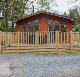 A wooden lodge with a fenced deck and outdoor furniture surrounded by trees at Oakwood Lodge Langdale 3 White Cross Bay Windermere