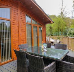 An outdoor deck with a glass table and wicker chairs outside a wooden cabin at Oakwood Lodge Langdale 3 White Cross Bay Windermere