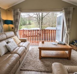 A living room with a leather sofa cushions coffee table rug and glass door opening to a balcony at Lakeland View Lodge Beckside 2 Limefitt Park near Windermere