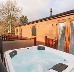 A hot tub on a wooden deck outside a lodge with trees and hills in the background at Lakeland View Lodge Beckside 2 Limefitt Park near Windermere