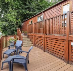 A wooden deck with steps and two black chairs and footrests outside a cabin at Acorn Bank Lodge L 55 Fallbarrow Park near Bowness-On-Windermere