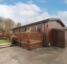 A wooden cabin with a porch and railing next to a driveway and garden at Damson Lodge Thirlmere 8 White Cross Bay Windermere