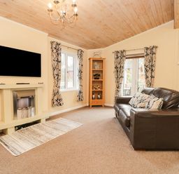 A living room with a brown leather sofa a fireplace a television on the wall patterned curtains and a wooden cabinet at Damson Lodge Thirlmere 8 White Cross Bay Windermere