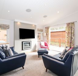 A living room with two blue sofas a pink chair a wall mounted television and floral curtains at Ridgway Lodge Calgarth 40 White Cross Bay near Windermere