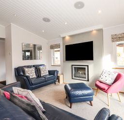 A living room with blue leather sofas a pink chair a wall-mounted tv and a fireplace at Ridgway Lodge Calgarth 40 White Cross Bay near Windermere