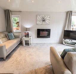 A living room with two sofas a wall-mounted fireplace a television on a stand and grey curtains at Buttermere Lodge Glade 5 Fallbarrow Park near Bowness on Windermere