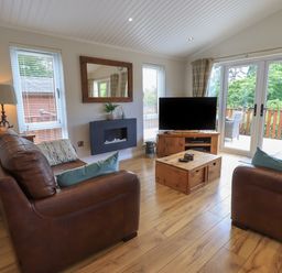 A living room with two brown leather sofas a wooden coffee table a wall-mounted fireplace and a television at Wansfell Retreat Lodge Wansfell 4 Limefitt Park near Windermere