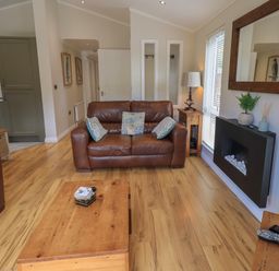 A living room with brown leather sofas a wooden coffee table a wall-mounted fireplace and a wooden mirror at Wansfell Retreat Lodge Wansfell 4 Limefitt Park near Windermere