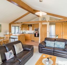 An open plan living room and kitchen with leather sofas a wooden dining table and kitchen cabinets at Sheffield Pike Lodge Ullswater 8 Limefitt Park near Windermere