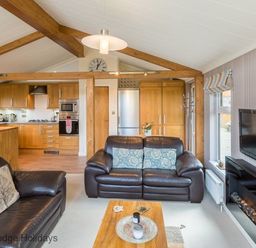 A living room with leather sofas wooden beams and a kitchen area at Sheffield Pike Lodge Ullswater 8 Limefitt Park near Windermere