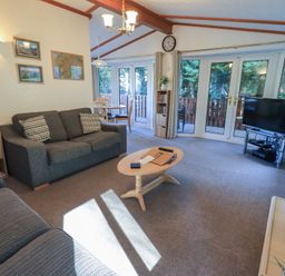 A living room with two sofas a coffee table a television and double glass doors opening to a balcony at Walkers Retreat Lodge in Fellside 5 Limefitt Park near Windermere