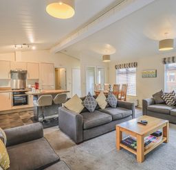 A living room with three sofas a wooden coffee table and a dining table next to an open kitchen at Daffodils Lodge Oakside 7 Fallbarrow Park in Bowness on Windermere