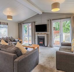A living room with two gray sofas a wooden coffee table a wall-mounted TV and a fireplace at Daffodils Lodge Oakside 7 Fallbarrow Park in Bowness on Windermere