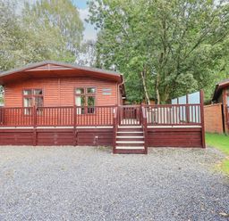 A wooden cabin with front stairs and railing surrounded by trees at Tanglewood Lodge Thirlmere 15 White Cross Bay near Windermere