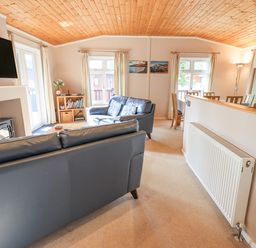 A living room with two black sofas a TV above a fireplace a bookshelf and a dining area at Tanglewood Lodge Thirlmere 15 White Cross Bay near Windermere