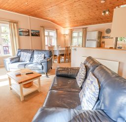 A living room with blue leather sofas a wooden coffee table a dining table with chairs and a kitchen area at Tanglewood Lodge in Thirlmere 15 White Cross Bay near Windermere