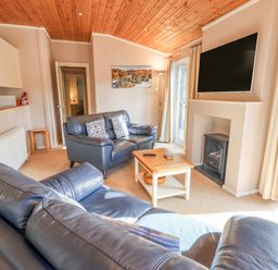 A living room with two leather sofas a wooden coffee table a wall-mounted television and a fireplace at Tanglewood Lodge Thirlmere 15 White Cross Bay near Windermere
