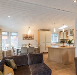 An open plan living area with a kitchen island dining table set and sofas at Broad Larch Lodge in Glade 16 Fallbarrow Park near Bowness on Windermere