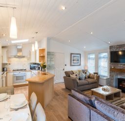 An open plan living room and kitchen with dining table sofas and television at Broad Larch Lodge in Glade 16 Fallbarrow Park near Bowness on Windermere