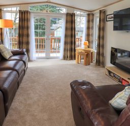 A living room with leather sofas a fireplace a wall-mounted tv and large windows at Squirrels Snug in Pony Meadow 1 White Cross Bay near Windermere