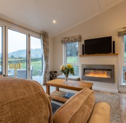 A living room with sofas a coffee table flowers in a vase a fireplace and a television at Comraich Beckside 40 Limefitt Park near Windermere