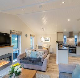 An open living room and kitchen with sofas flowers and a dining table at Comraich Beckside 40 Limefitt Park near Windermere