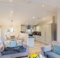 An open living area with two sofas and a dining table next to a kitchen with cream cabinets at Comraich Beckside 40 Limefitt Park near Windermere