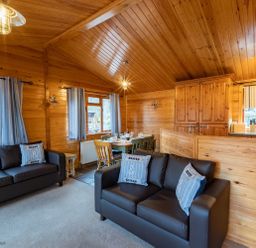 A living room with two black sofas and pillows next to a dining table and wooden kitchen cabinets at Lakeshaven Skiptory Howe 16 White Cross Bay near Windermere