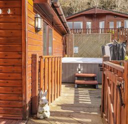 A wooden deck with a hot tub steps and a welcoming rabbit statue at Limefitt Lodge Fellside 8 Limefitt Park near Windermere