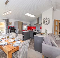 A kitchen and dining area with a wooden table set for six and a gray sofa at Limefitt Lodge Fellside 8 Limefitt Park near Windermere