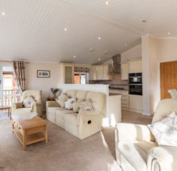 A living room with beige sofas and a wooden coffee table next to a kitchen with white cabinets at Waterbird in Lakeview 4 White Cross Bay near Windermere