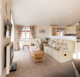 A living room with sofas coffee table wall-mounted TV and kitchen in the background at Waterbird Lakeview 4 White Cross Bay near Windermere