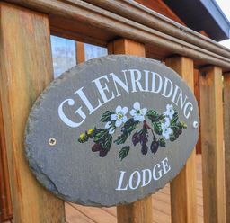 A wooden railing with a stone sign reading Glenridding Lodge with painted flowers at Glenridding Lodge Grasmere 2 White Cross Bay near Windermere