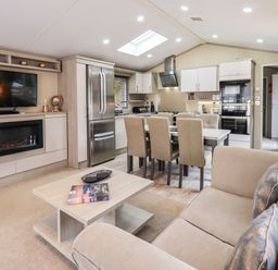 An open plan living room and kitchen with sofa, dining table with six chairs, refrigerator, and television at Glenridding Lodge in Grasmere 2 White Cross Bay near Windermere