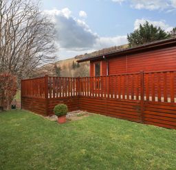 A wooden deck attached to a building with green grass and trees surrounding it at Wainwright Lodge Kirkstone 27 Limefitt Park near Windermere