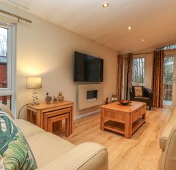 A living room with two beige sofas wooden coffee tables a wall-mounted TV and a window with a view at Wainwright Lodge Kirkstone 27 Limefitt Park near Windermere