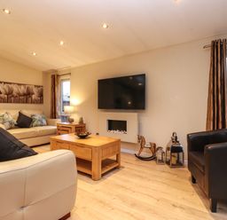 A living room with cream sofas dark armchair wooden coffee table and wall mounted TV at Wainwright Lodge Kirkstone 27 Limefitt Park near Windermere