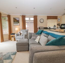 A living room with a grey couch and armchair next to a kitchen area at Pheasant's Nest Kirkstone 11 Limefitt Park near Windermere
