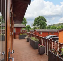 A wooden balcony with planters and a view of wooden cabins and trees at Pheasant's Nest Kirkstone 11 Limefitt Park near Windermere
