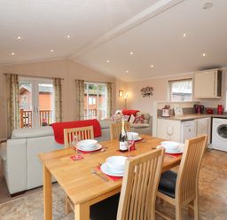 An open kitchen and dining area with a wooden dining table set for four people and a living room with white sofas and red cushions at Robins Nest Bowness 71 White Cross Bay near Windermere