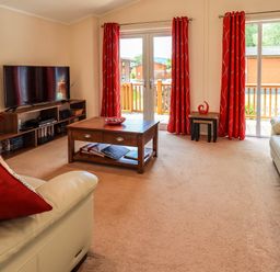 A living room with two white sofas with red cushions a wooden coffee table and entertainment unit with a tv at Robin's Nest in Bowness 71 White Cross Bay near Windermere