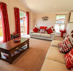 A living room with two beige sofas red cushions a wooden coffee table and red curtains at Robins Nest Bowness 71 White Cross Bay near Windermere