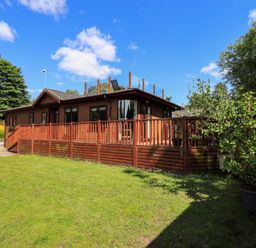 A wooden house with a raised deck and glass railings on the roof surrounded by grass and trees at Thirlmere View Thirlmere 6 White Cross Bay near Windermere