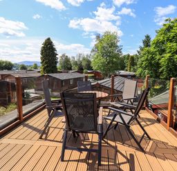 An outdoor wooden deck with six chairs and a round table surrounded by glass panels at Thirlmere View Thirlmere 6 White Cross Bay near Windermere